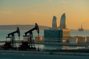 High-angle dusk photo from a rooftop in Baku: illuminated glass bank tower in foreground,